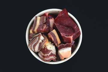 Top view of dog bowl with big red chunks of meat with fat used for dog or cat raw biologically appropriate feeding on black background