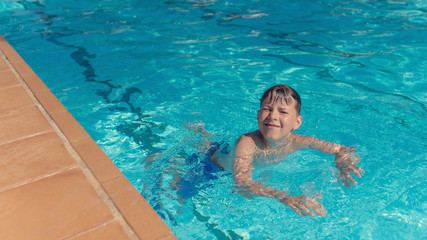 Portrait of smiling Caucasian boy spending time in pool at resort.  He is swimming in water and enjoying his summer vacations.