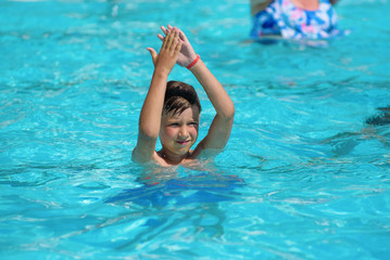 Smiling Caucasian boy having fun in swimming pool at resort. He dancing aqua Zumba and claping hands.