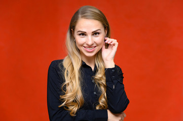 Portrait of a pretty blonde financial secretary girl with long curly hair in a business suit standing in the studio on a red background with emotions in different poses.