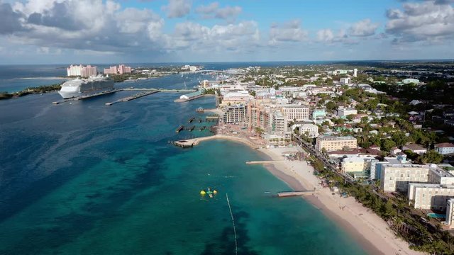 Aerial: Nassau Cityscape, Beach, Hotels, and Huge Cruise Ship Docked Near Shore