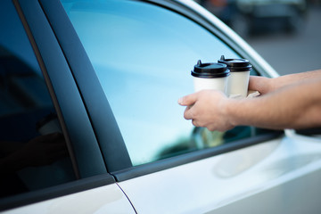 Fototapeta na wymiar hands of a man who holds out coffee in paper cups to a man in a car