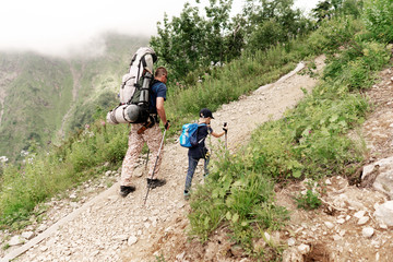 Father helps little son to go on his first mountain trip. Climb the mountain trail. The concept of family education and parenthood. Ecological sports rest.