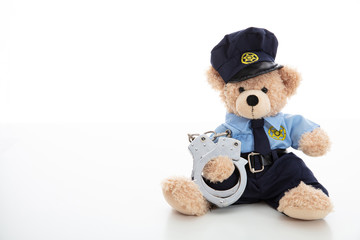 Cute teddy in policeman uniform and handcuffs isolated against white background