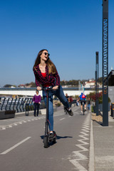 Pretty young woman riding an electric scooter in the street
