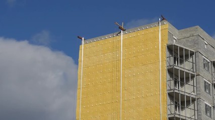 Thermal insulation technology of a large residential building. Wall of a large house with a heater made of special glass wool against a blue sky, close-up