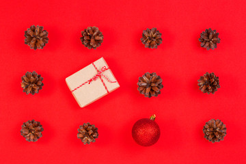 Christmas composition. Pattern made of pine cones, christmas decoration and gift box on red background. Top view, flat lay