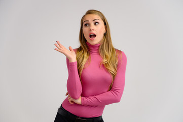 Close-up portrait of a pretty blonde girl with long curly hair standing in the studio on a white background with emotions in different poses in a pink sweater. Beauty, Model, Cosmetics