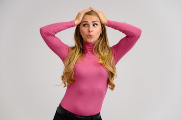 Close-up portrait of a pretty blonde girl with long curly hair standing in the studio on a white background with emotions in different poses in a pink sweater. Beauty, Model, Cosmetics