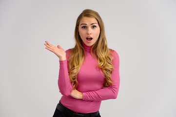 Close-up portrait of a pretty blonde girl with long curly hair standing in the studio on a white background with emotions in different poses in a pink sweater. Beauty, Model, Cosmetics