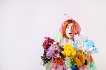 Emotional redhead woman looking stressed, covered with eco harmful plastic garbage, bags and straws of different color. Zero waste concept. Sad female frowning, angry about littering.