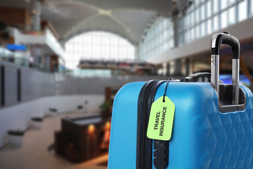 Blue suitcase with TRAVEL INSURANCE label in airport terminal
