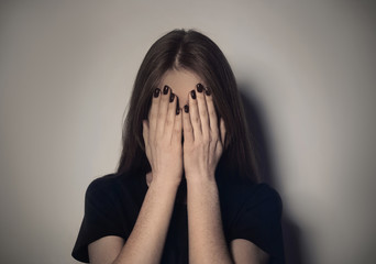 Upset young woman crying against light background