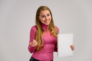 Close-up portrait of a pretty blonde girl with long curly hair standing in the studio on a white background with emotions in different poses in a pink sweater with a folder in her hands.