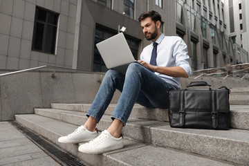Handsome man working with laptop on city street