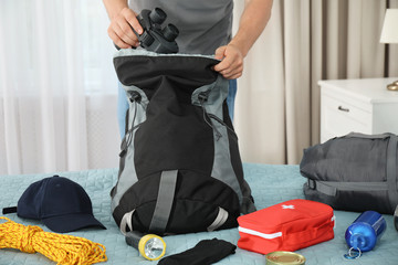 Man packing different camping equipment into backpack at home, closeup
