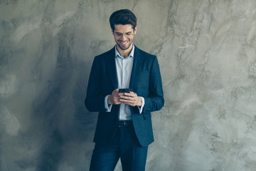 Portrait of positive cheerful ceo worker using smartphone send sms to colleagues having fun on his workplace wearing stylish pants isolated over grey color background