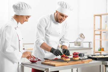 Pastry chefs preparing desserts at table in kitchen