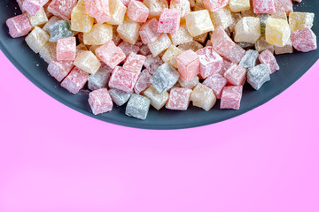 Turkish delight multicolored on a dark blue plate on a white background.