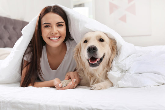 Young woman and her Golden Retriever dog on bed at home