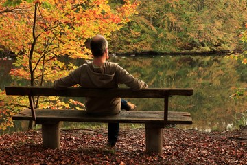 Fototapeta premium man sitting alone on a park bench in beautiful fall landscape by the river
