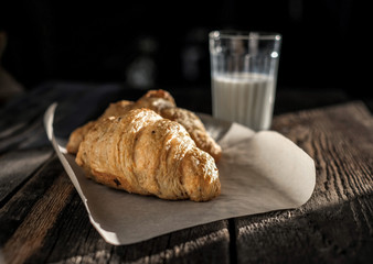 Delicious breakfast with fresh croissants and glass of milk on wooden table at sun light