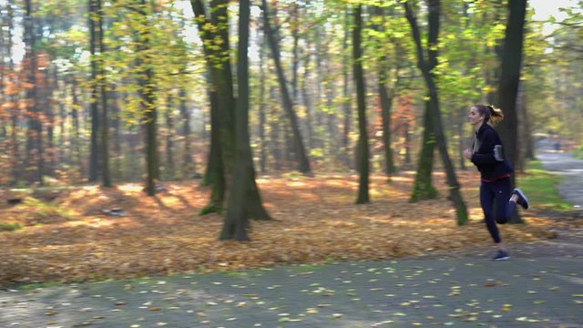 Woman with earphones running in park during autumn