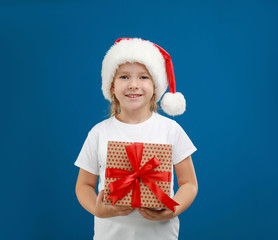 Cute little child wearing Santa hat with Christmas gift on blue background