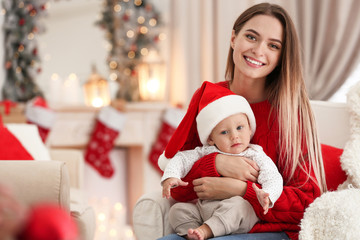 Happy mother with cute baby in room decorated for Christmas holiday