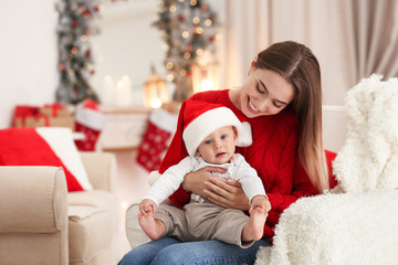 Happy mother with cute baby in room decorated for Christmas holiday