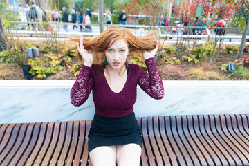 Young woman playing with her red hair while sitting outside on a bench