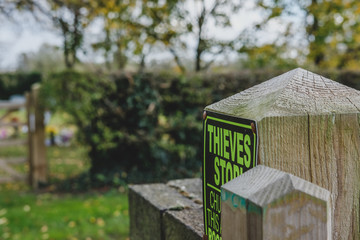 Shallow focus view of a theft prevention sign seen attached to an entrance to a rural cemetery and church yard, in late autumn.