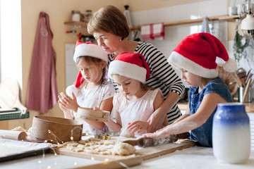 Family is cooking Christmas gingerbread cookies together in cozy home kitchen for dinner. Kids and grandmother prepare homemade holiday food. Girls help woman. Lifestyle moment. Children chef concept