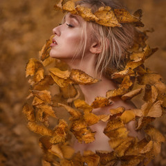 Autumn portrait. A girl with a long neck wrapped in a hurricane of yellow leaves reaches up closing...