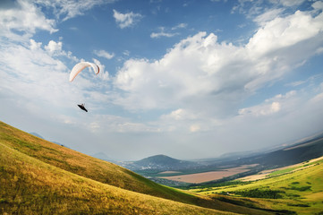 A paraglider flies in the sky in a cocoon suit on a paraglider over the Caucasian countryside with...