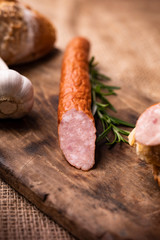 Smoked pork sausage in composition with fresh herbs, bread, wood cutting board and jute fabric.
