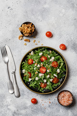 Healthy vegetable salad with fresh arugula, tomato, feta cheese and walnut on dark plate. Diet menu. Top view. Salad with arugula 
