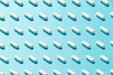 Trendy pattern made with Pharmaceutical medicine pills, tablets and capsules on bright light blue background. Medicine creative concepts. Minimal style with colorful paper backdrop. Trendy colors