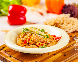 Noodles with vegetables and chicken in beige plate on wooden board