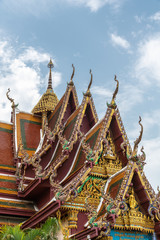 Fototapeta premium Ko Samui Island, Thailand - March 18, 2019: Wat Laem Suwannaram Chinese Buddhist Temple. Elaborately gold decorated full of colors front gables with several statues under blue cloudscape.