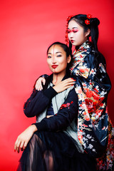 two pretty geisha girls friends: modern asian woman and traditional wearing kimono posing cheerful on red background