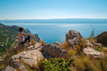 Young woman is sitting on the top of mountain and enjoying the view