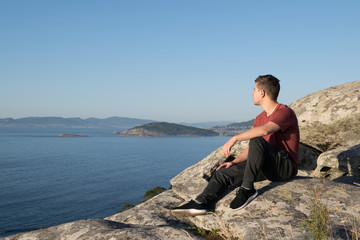 Fototapeta premium Boy sitting on the rocks of a mountain looking at the ocean