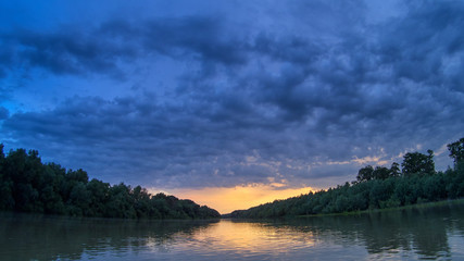 Beautiful bright dramatic sunset over Danube river with forest along riverside