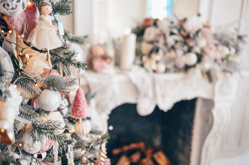 Christmas decorated tree in soft pink colors against the background of white classic fireplace with Christmas decorations.  Fragment of New Year festive living room interior