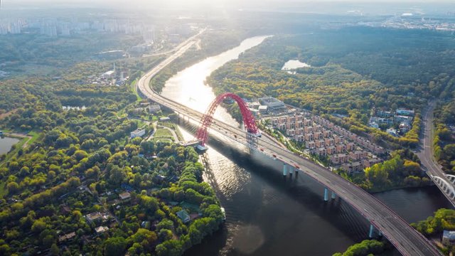 Amazing aerial panorama of red Picturesque bridge over the Moscow river. Camera moving around showing large arch of the bridge in beautiful summer landscape and its road traffic in motion timelapse.