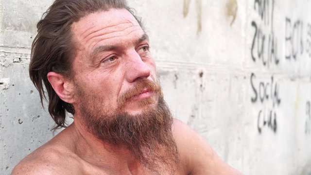 Bearded destitute man sits on the street and talks