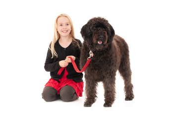 Young blonde girl holding black labradoodle on a red leash. Isolated on white studio background