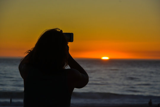 Silhouette of woman taking a picture with mobile at sunset on the beach