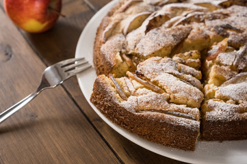 Homemade apple pie on the plate with a fork and apple on the wooden background
